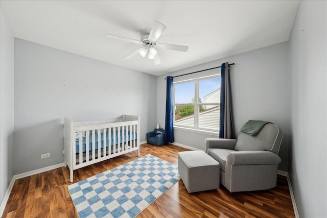 bedroom featuring baseboards, ceiling fan, wood finished floors, and a crib