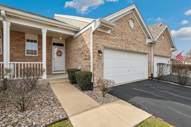 view of front of property with aphalt driveway, brick siding, an attached garage, and covered porch
