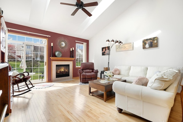 living area with light wood-style floors, high vaulted ceiling, ceiling fan, and a tiled fireplace