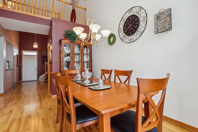 dining space featuring light wood-style flooring, a towering ceiling, a notable chandelier, and baseboards