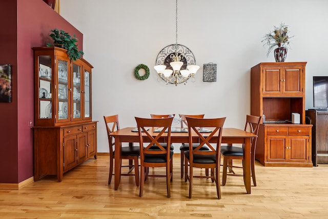dining space featuring light wood-style floors, a notable chandelier, baseboards, and a towering ceiling