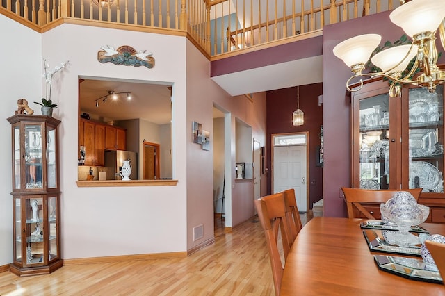 dining room featuring an inviting chandelier, a towering ceiling, visible vents, light wood finished floors, and baseboards