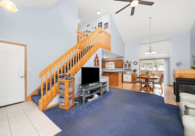 living area featuring high vaulted ceiling, stairway, a chandelier, and a ceiling fan