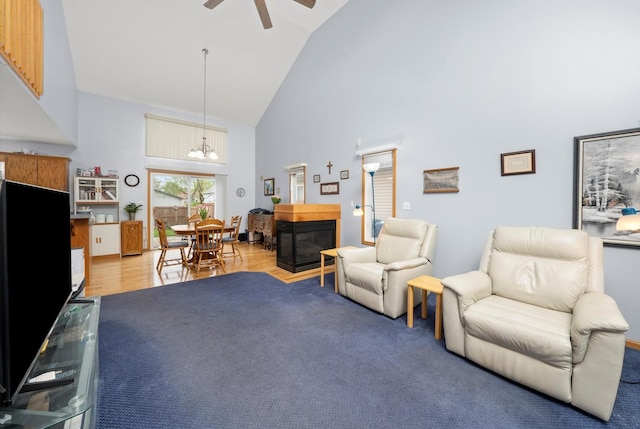 living room featuring high vaulted ceiling, a ceiling fan, a chandelier, a glass covered fireplace, and light wood finished floors