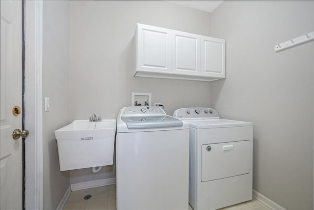 clothes washing area with cabinet space, washer and clothes dryer, baseboards, and a sink