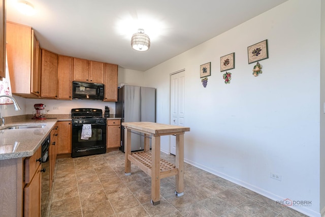 kitchen featuring baseboards, light stone counters, a sink, and black appliances