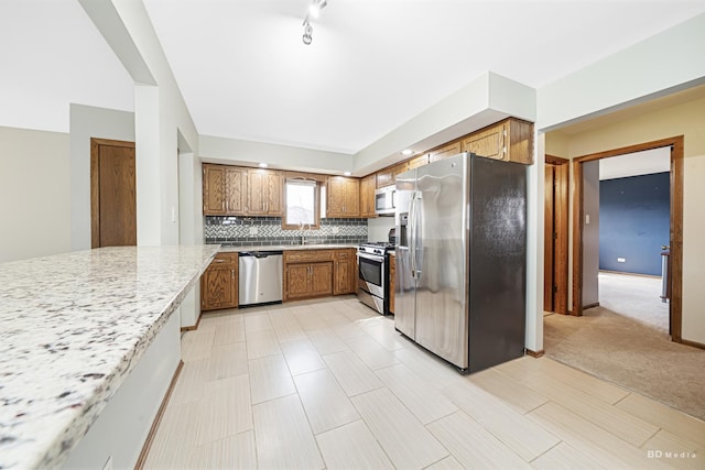 kitchen with light stone countertops, brown cabinetry, tasteful backsplash, a sink, and stainless steel appliances