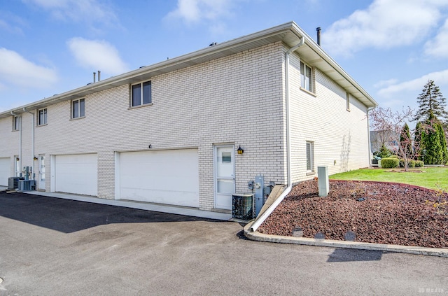 view of side of home featuring an attached garage, central AC, aphalt driveway, and brick siding