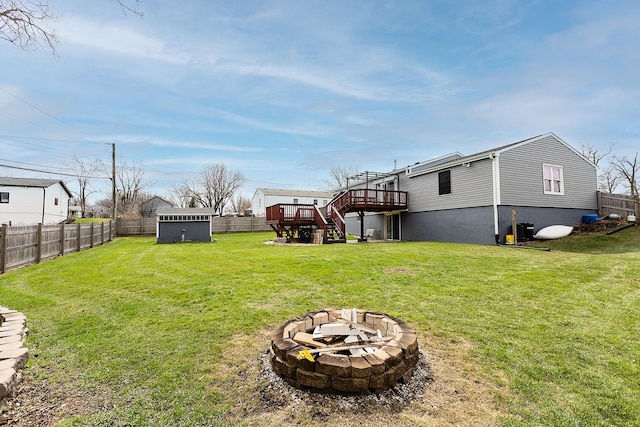 view of yard featuring an outbuilding, a wooden deck, a fenced backyard, a fire pit, and stairs