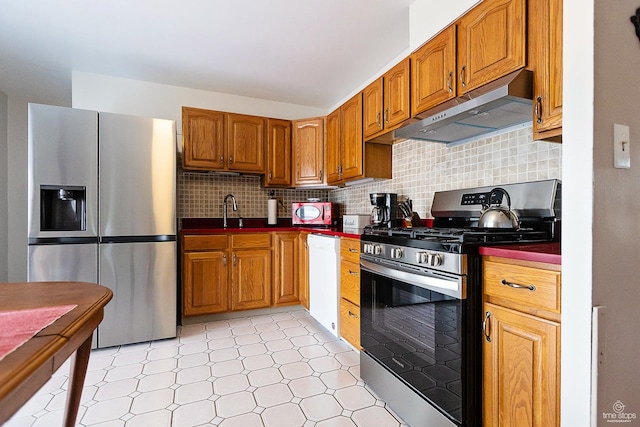 kitchen featuring dark countertops, under cabinet range hood, brown cabinets, stainless steel appliances, and decorative backsplash