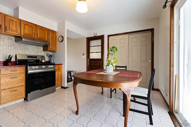 kitchen featuring plenty of natural light, under cabinet range hood, brown cabinetry, backsplash, and stainless steel gas range oven