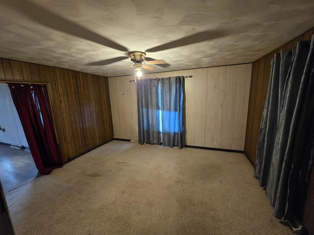 empty room featuring baseboards, a ceiling fan, wood walls, and light carpet