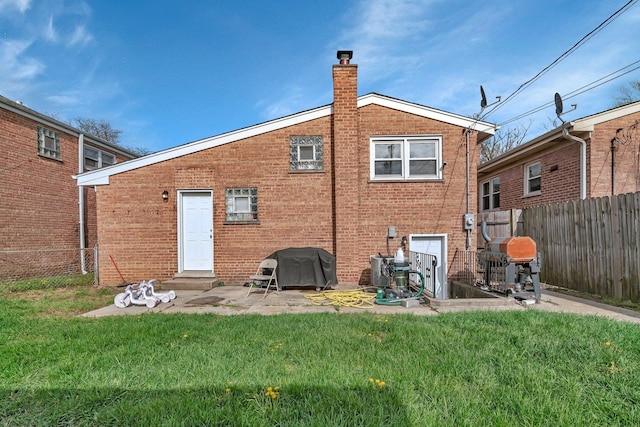 rear view of house with fence, a chimney, brick siding, and a yard