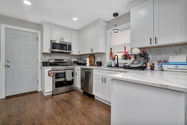 kitchen with white cabinets, stainless steel appliances, a sink, backsplash, and light stone counters
