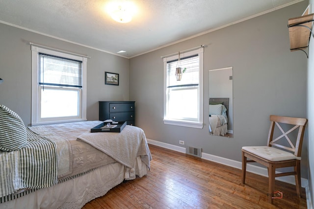 bedroom featuring wood-type flooring, baseboards, ornamental molding, and visible vents