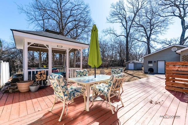 wooden deck featuring a storage shed, an outbuilding, a gazebo, fence, and outdoor dining area