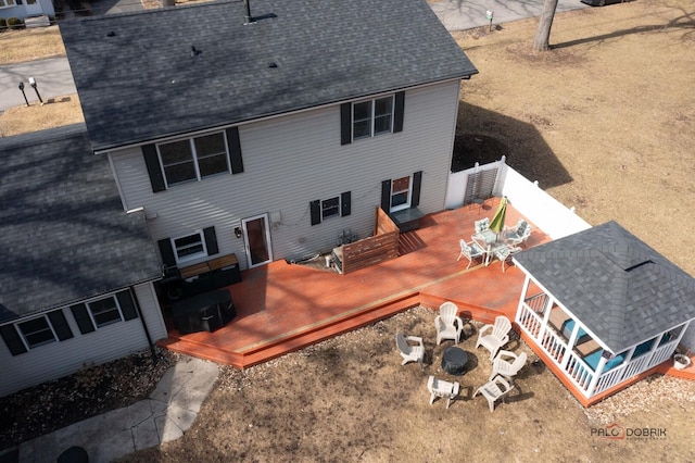rear view of house with a wooden deck, roof with shingles, and an outdoor fire pit