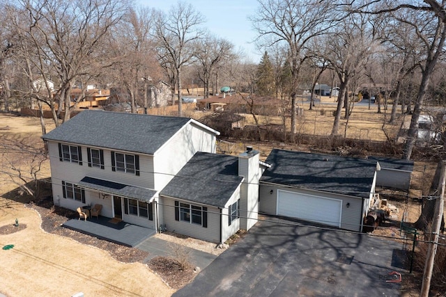 traditional-style house featuring an attached garage, driveway, roof with shingles, and a chimney