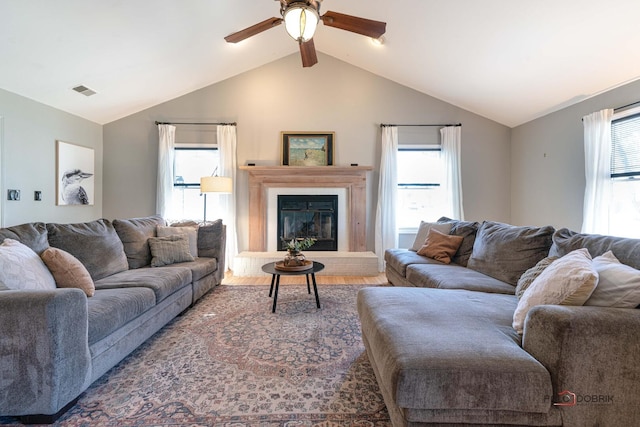 living room featuring wood finished floors, vaulted ceiling, a glass covered fireplace, and ceiling fan