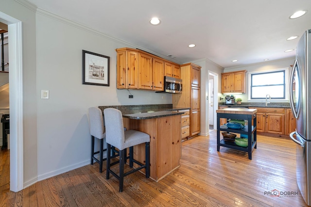 kitchen featuring ornamental molding, a peninsula, light wood-style flooring, appliances with stainless steel finishes, and a breakfast bar area