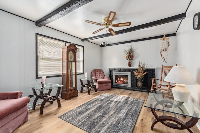 sitting room with baseboards, ceiling fan, beam ceiling, wood finished floors, and a glass covered fireplace