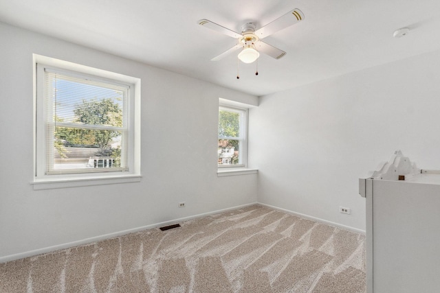 empty room with visible vents, baseboards, a ceiling fan, and light colored carpet