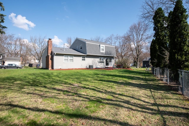 rear view of house with roof with shingles, a chimney, a yard, a gambrel roof, and fence