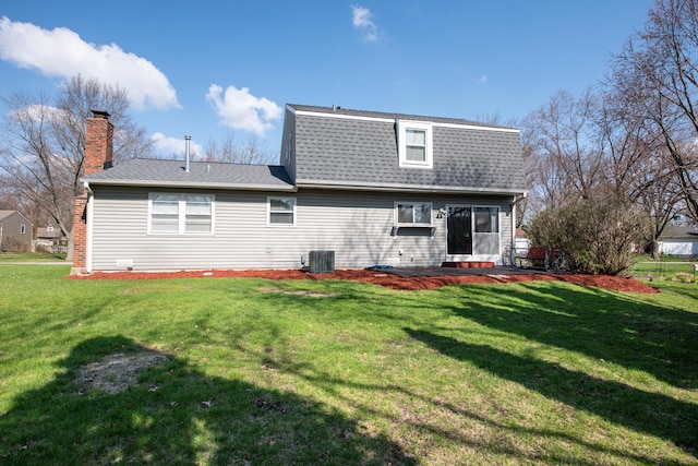 back of house featuring central air condition unit, a shingled roof, a lawn, and a chimney