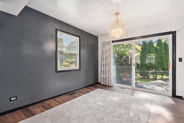 spare room with a notable chandelier, visible vents, and wood finished floors