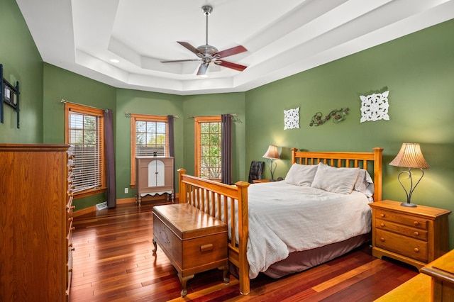 bedroom featuring a ceiling fan, a tray ceiling, baseboards, visible vents, and wood-type flooring