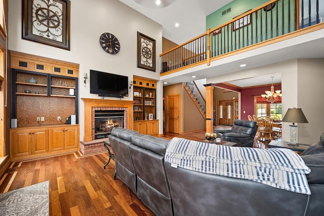 living room featuring stairs, a brick fireplace, a chandelier, wood finished floors, and a high ceiling