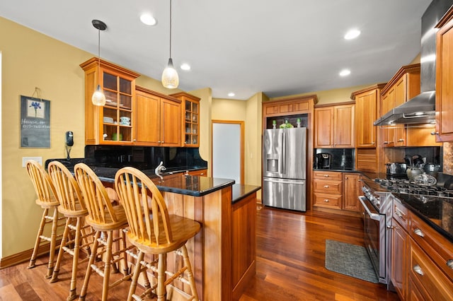 kitchen with brown cabinets, a peninsula, appliances with stainless steel finishes, and tasteful backsplash