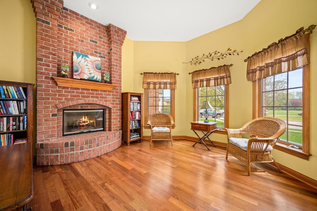 living area featuring a towering ceiling, a brick fireplace, baseboards, and wood finished floors