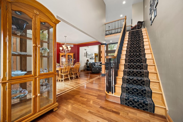 stairway with an inviting chandelier, visible vents, a towering ceiling, and wood finished floors
