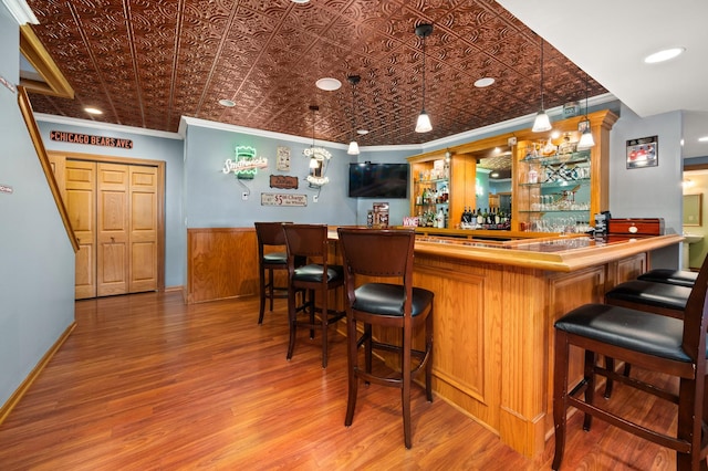 bar with an ornate ceiling, bar area, ornamental molding, hanging light fixtures, and wood finished floors