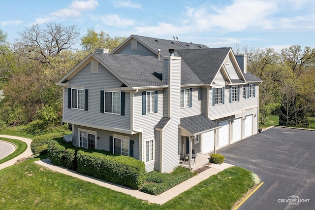 multi unit property featuring a chimney, a shingled roof, asphalt driveway, an attached garage, and a front lawn