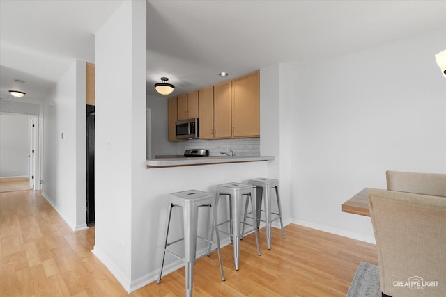 kitchen featuring stainless steel microwave, light wood finished floors, a breakfast bar area, tasteful backsplash, and baseboards