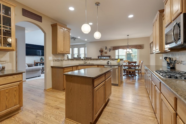 kitchen with appliances with stainless steel finishes, a sink, a peninsula, light wood-style floors, and a kitchen island