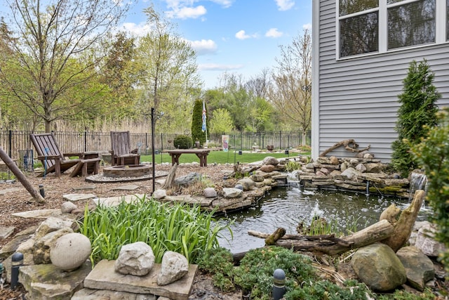 view of yard featuring fence, a small pond, and an outdoor fire pit