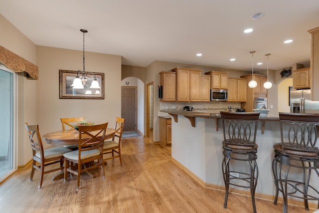 kitchen featuring appliances with stainless steel finishes, arched walkways, a breakfast bar, light wood-style flooring, and recessed lighting