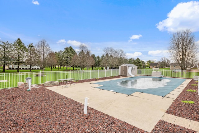 view of pool featuring a shed, a fenced backyard, a water slide, an outdoor structure, and a patio