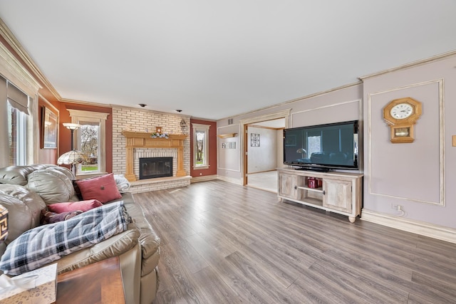 living room with crown molding, a brick fireplace, wood finished floors, and baseboards