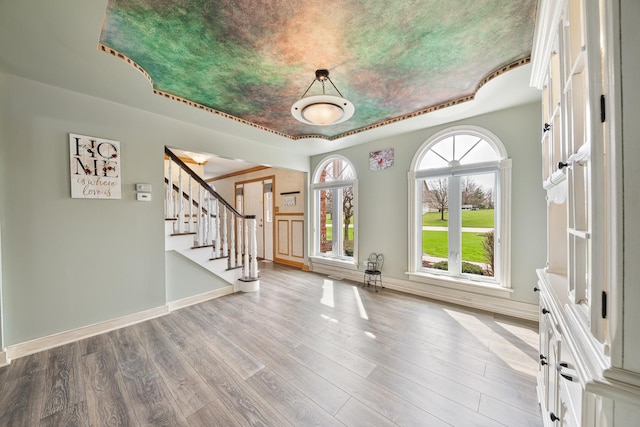 interior space featuring stairway, a tray ceiling, baseboards, and wood finished floors