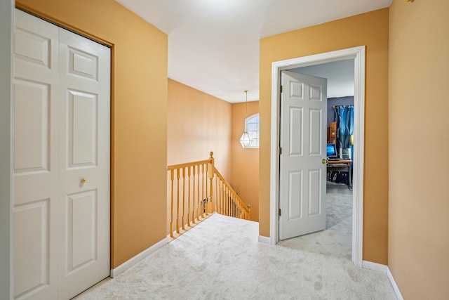 hall featuring carpet floors, baseboards, and an upstairs landing