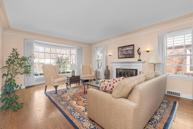 living room featuring ornamental molding, wood-type flooring, a glass covered fireplace, and visible vents