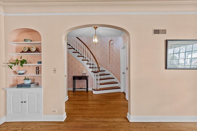interior space featuring visible vents, baseboards, crown molding, stairway, and wood finished floors
