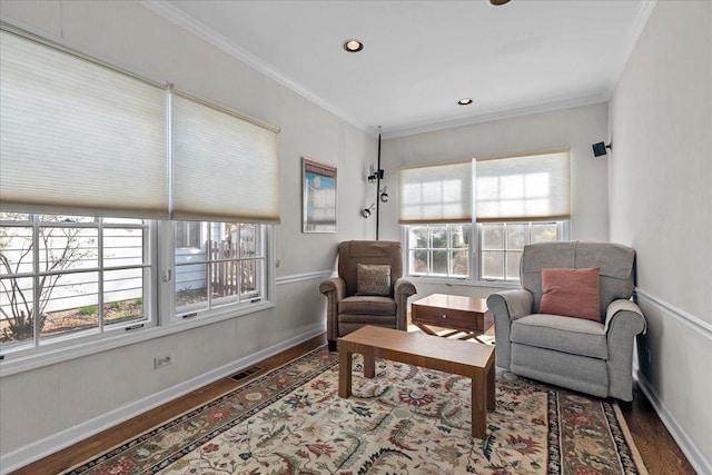 sitting room with ornamental molding, baseboards, wood finished floors, and a healthy amount of sunlight