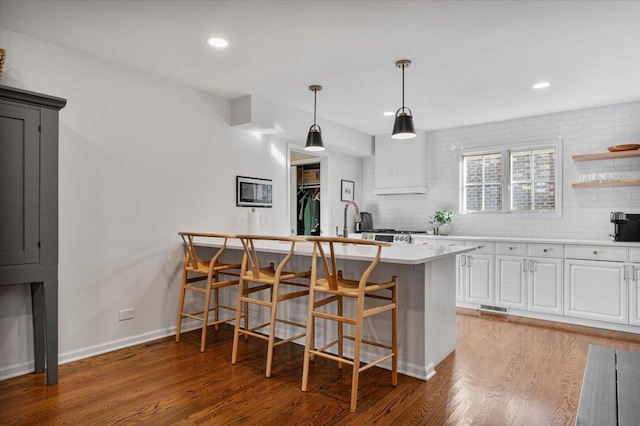kitchen featuring tasteful backsplash, a breakfast bar, white cabinetry, light wood-style flooring, and light countertops