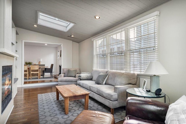 living room featuring dark wood-style floors, recessed lighting, lofted ceiling with skylight, and a glass covered fireplace
