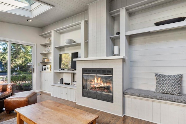 living area with a skylight, a tile fireplace, wood finished floors, built in shelves, and baseboards